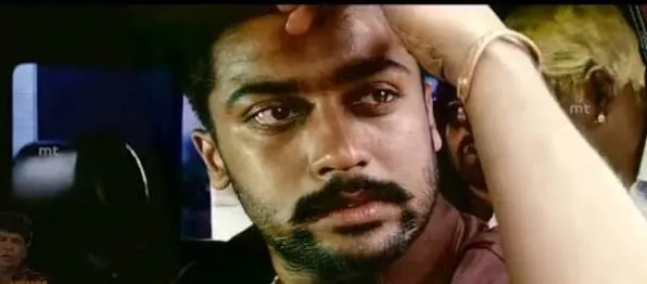 Suriya with a thick mustache looking shocked and emotional inside an automobile