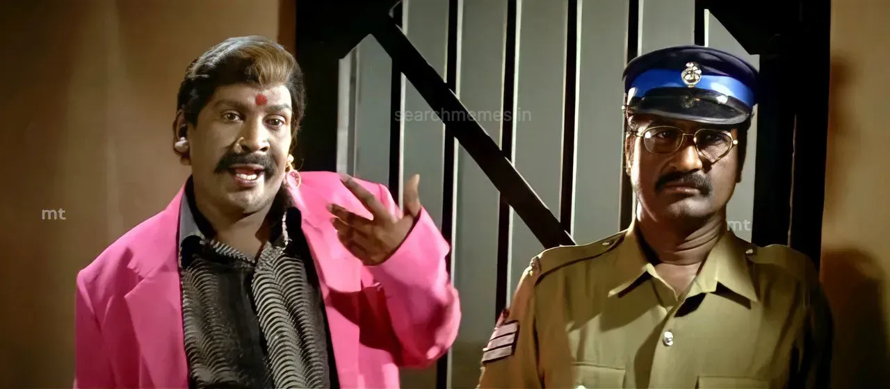 Vadivelu in a bright pink coat standing proudly beside a police officer