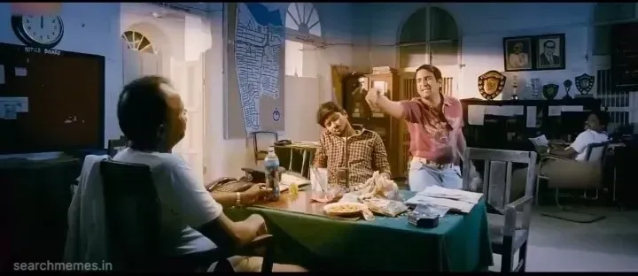 Santhanam in a police station, looking tired and pointing at a clock showing 12 o'clock, asking if the situation will end.