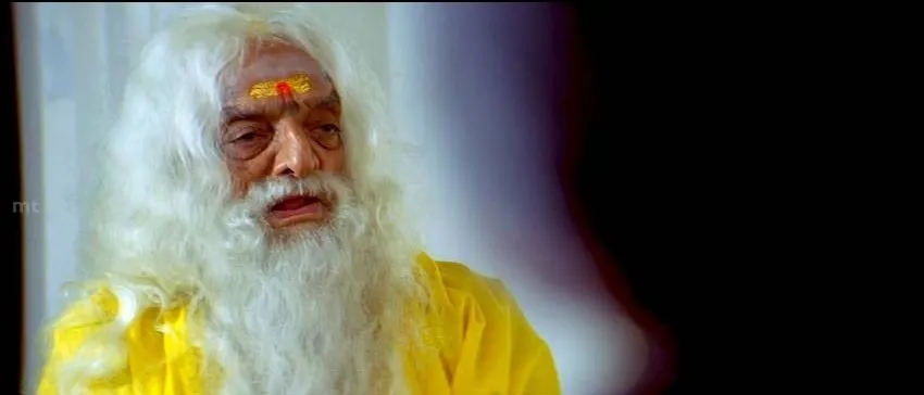 Elderly priest with white beard and yellow robes speaking with serious expression