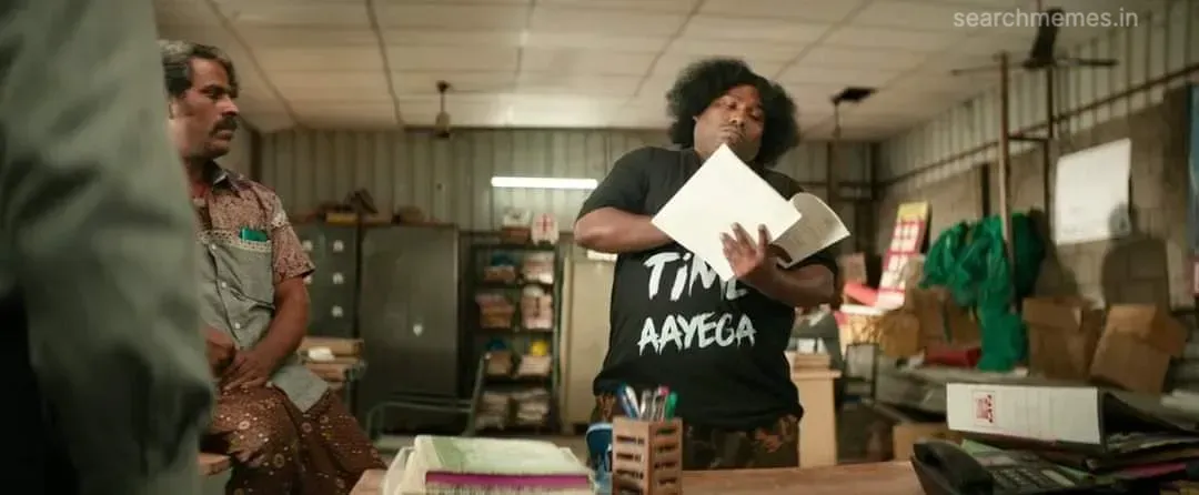 Yogi Babu flipping through papers in an office, wearing a printed black T-shirt