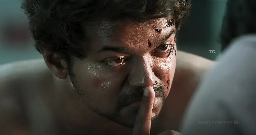 Close-up of bruised Vijay pressing an index finger to his lips demanding quiet