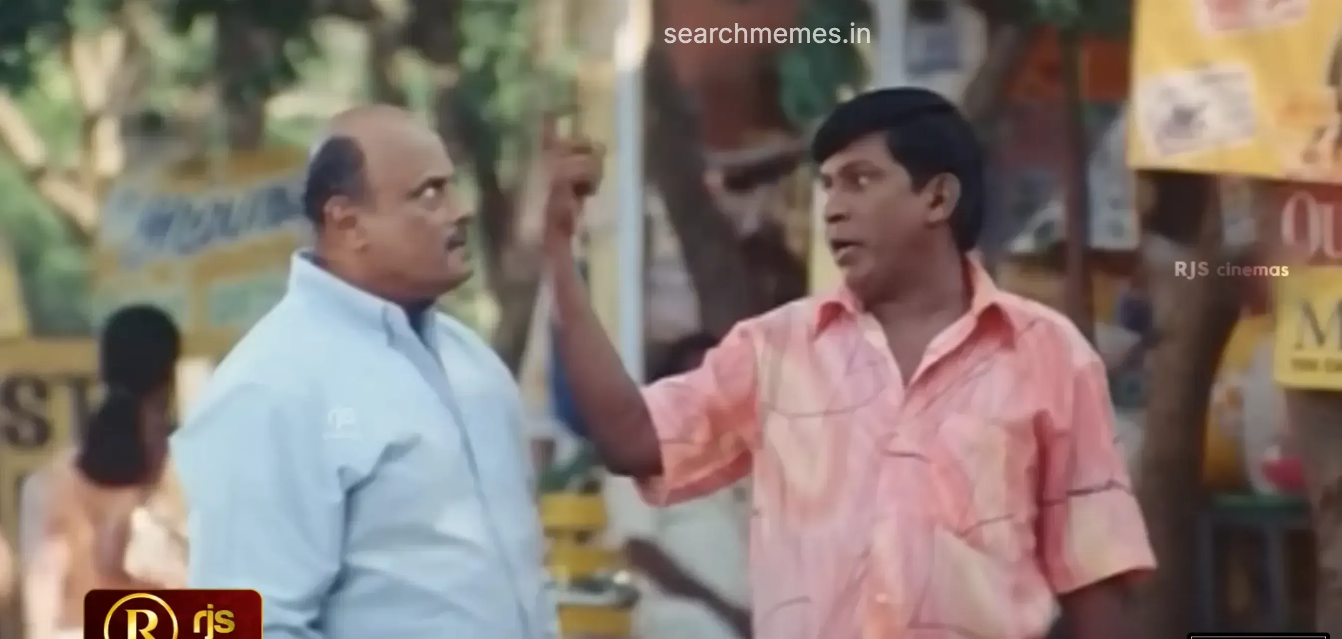 Vadivelu pointing an index finger upward and warning a bald man outdoors