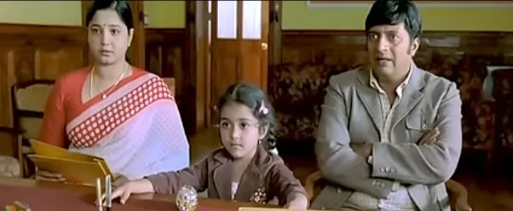 Prakash Raj sitting with arms crossed looking baffled beside his family in an office