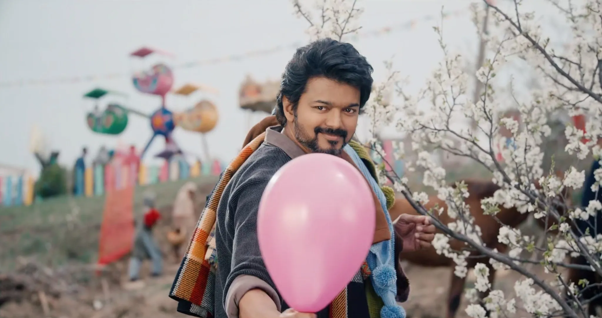 Vijay holding out pink balloon towards camera with subtle playful smile