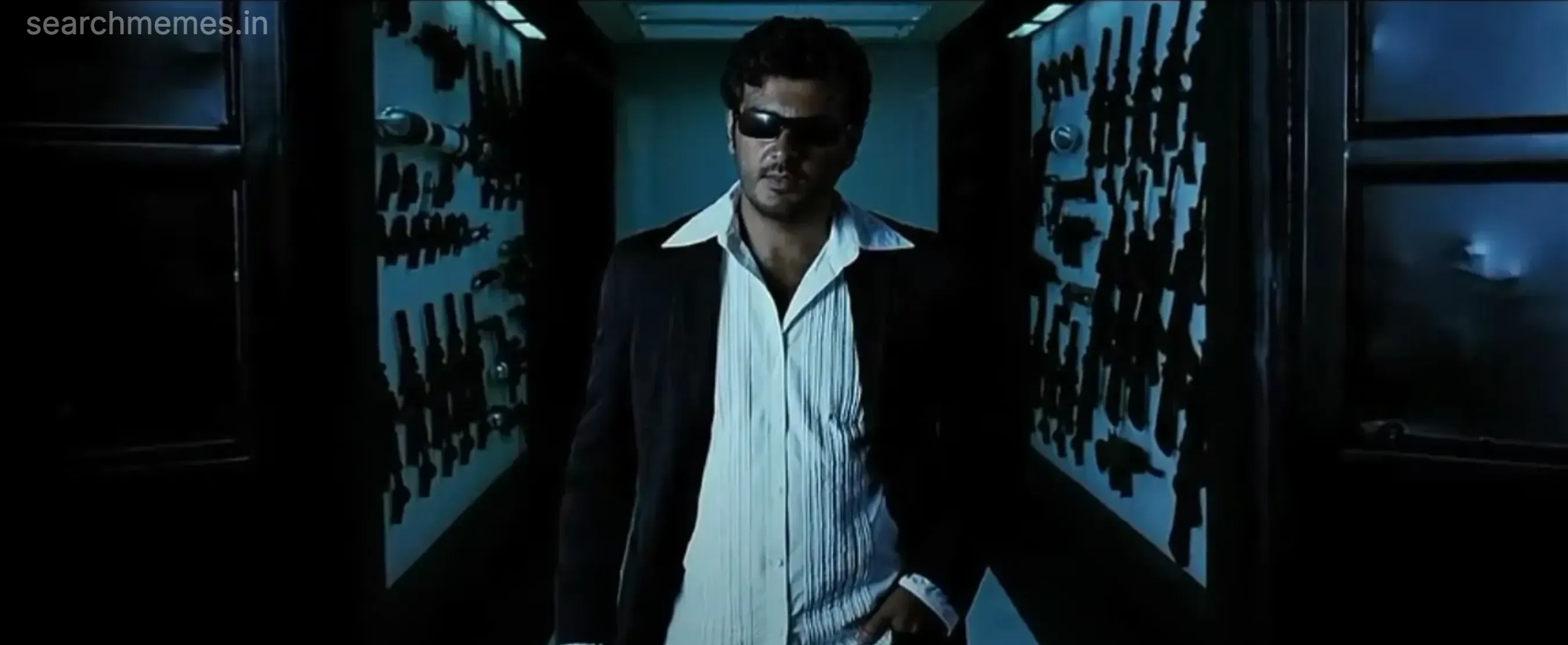 Ajith Kumar in formal blazer and sunglasses walking through corridor lined with weapons