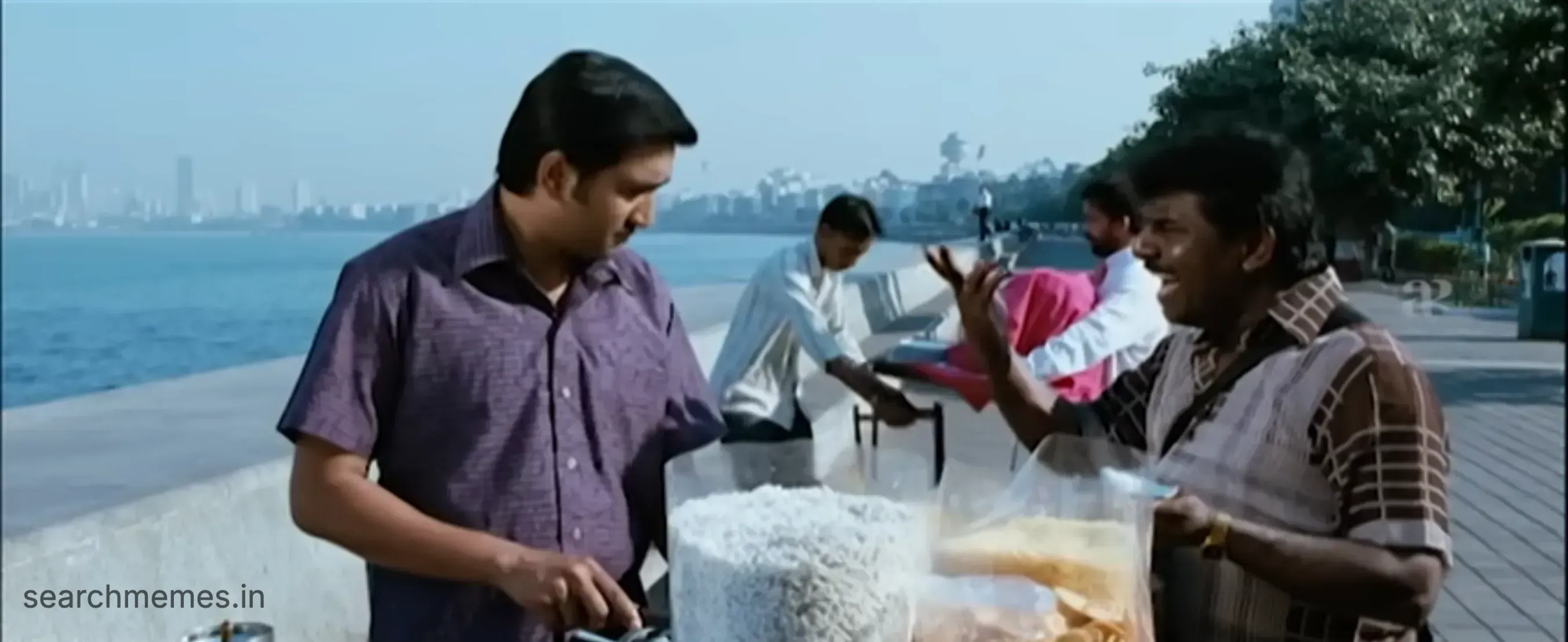 Santhanam gesturing dramatically while talking to a man by a beachside food stall