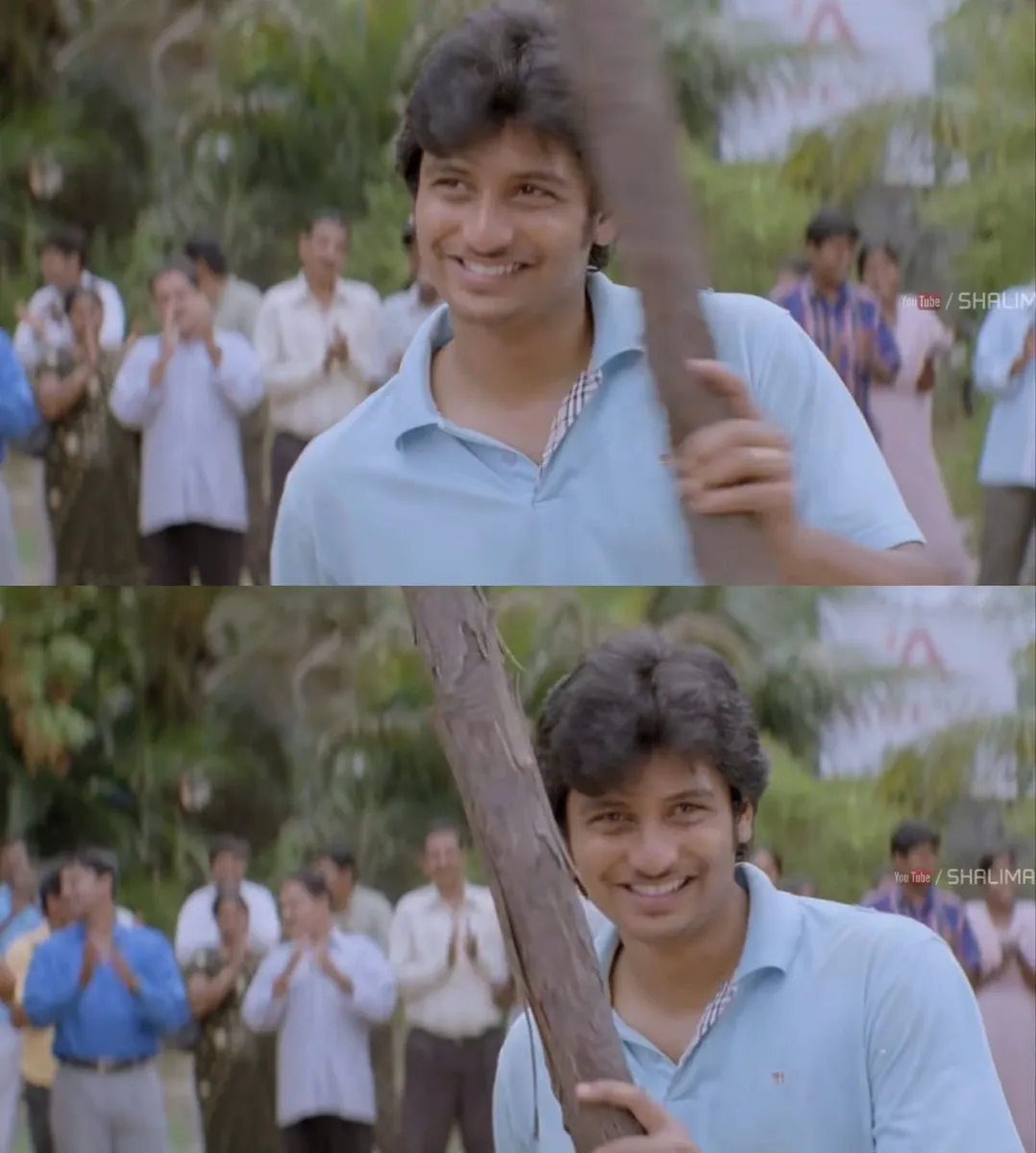 Jiiva holding a thick club horizontally behind his neck with proud smirk