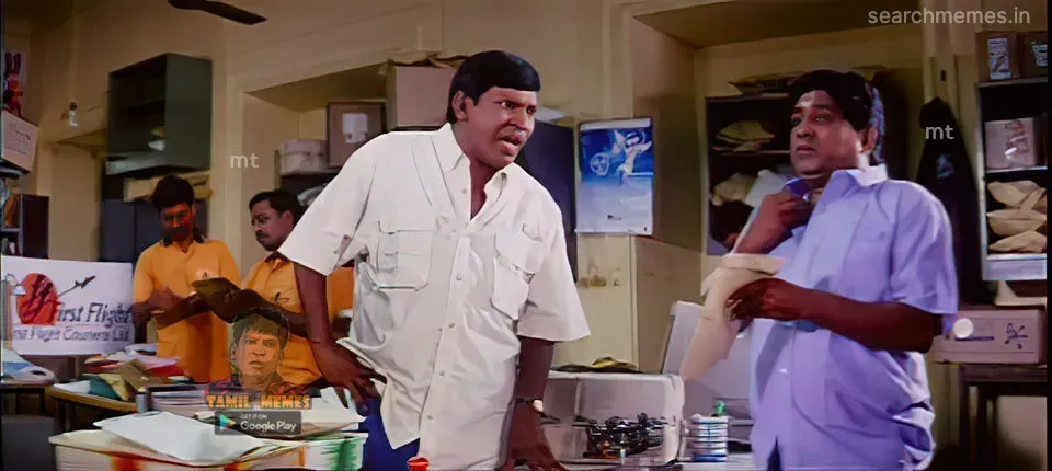 Vadivelu leaning over an office desk looking annoyed at Singamuthu