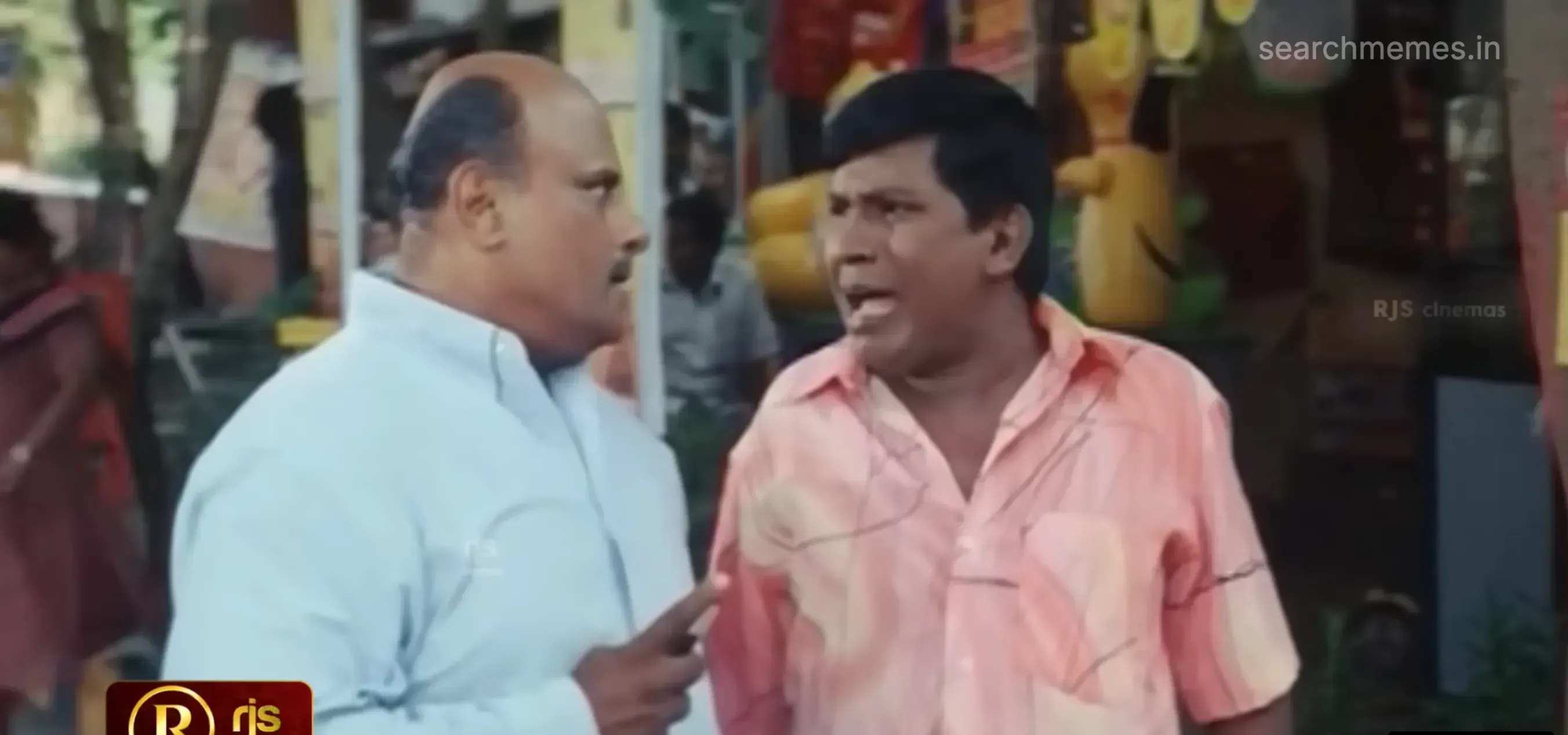 Vadivelu in a peach shirt animatedly lecturing a bald man on a street