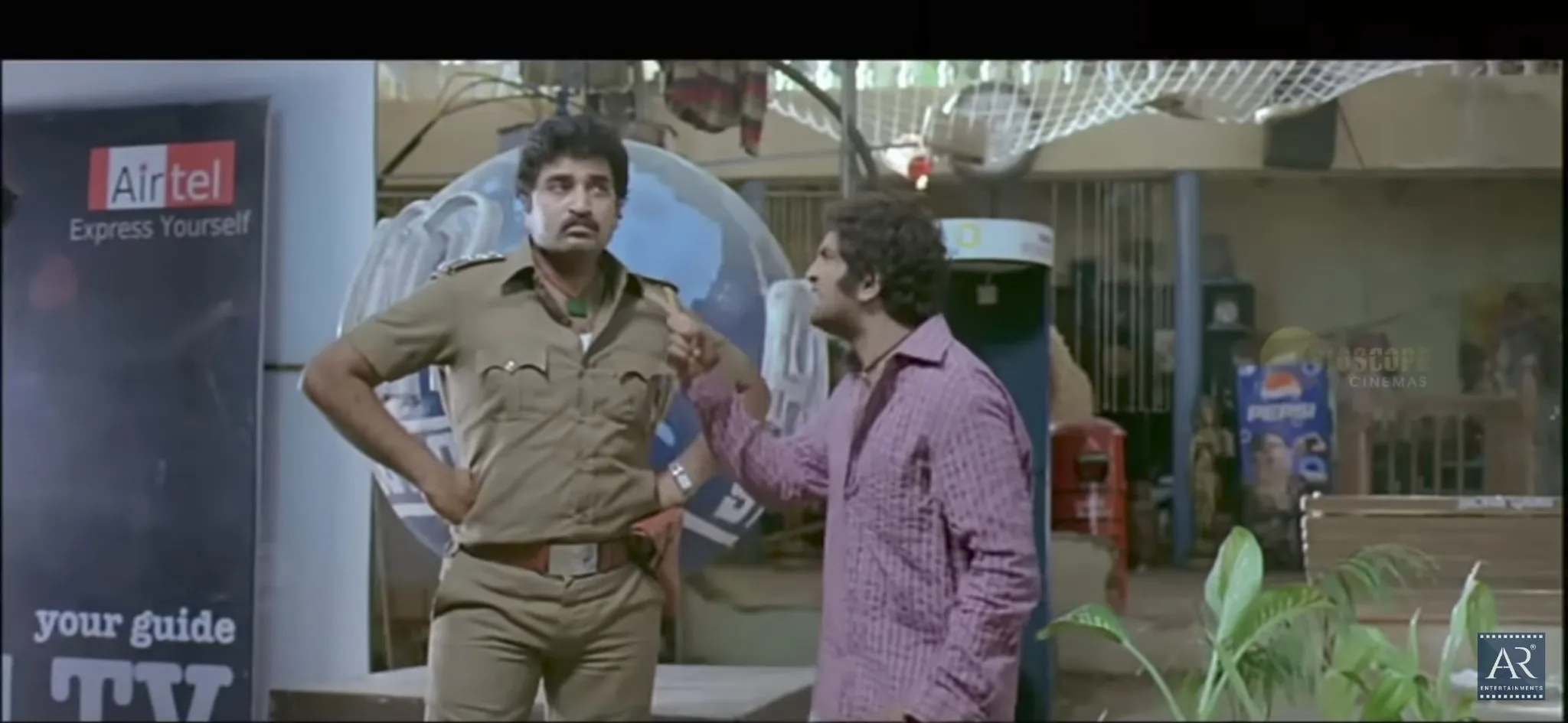 Santhanam pointing and explaining himself to a police inspector in Siruthai