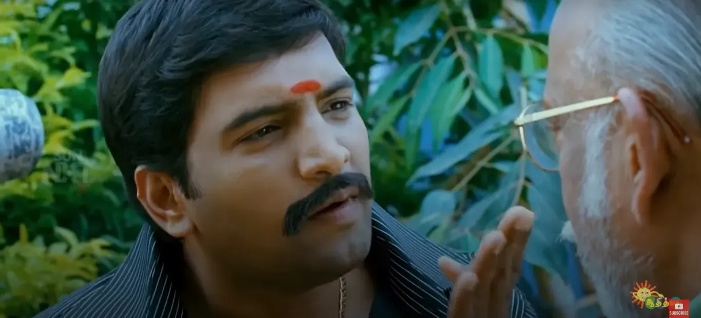 Santhanam with a tilak staring closely at an older man with glasses