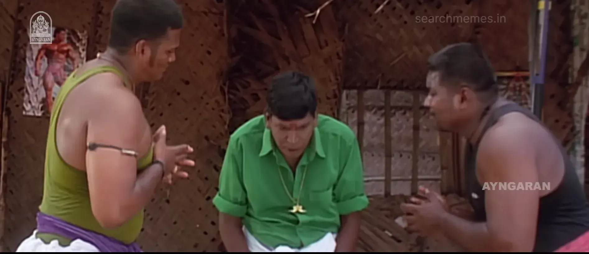 Vadivelu in a green shirt bowing his head humbly before two muscular men