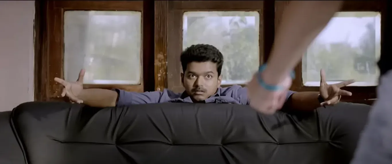 Vijay ducking behind a sofa with both hands stretched out in astonishment