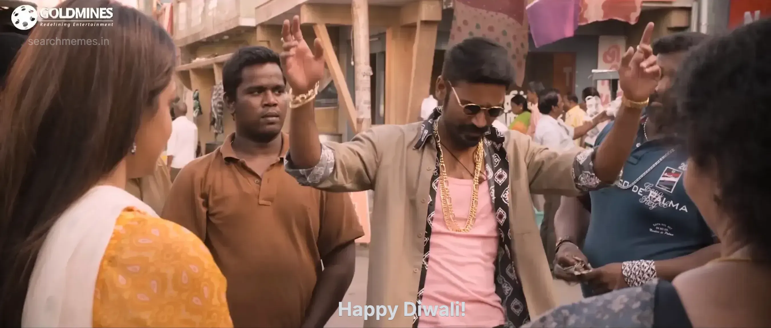Dhanush wearing sunglasses and gold chains waving his hands in a crowded street