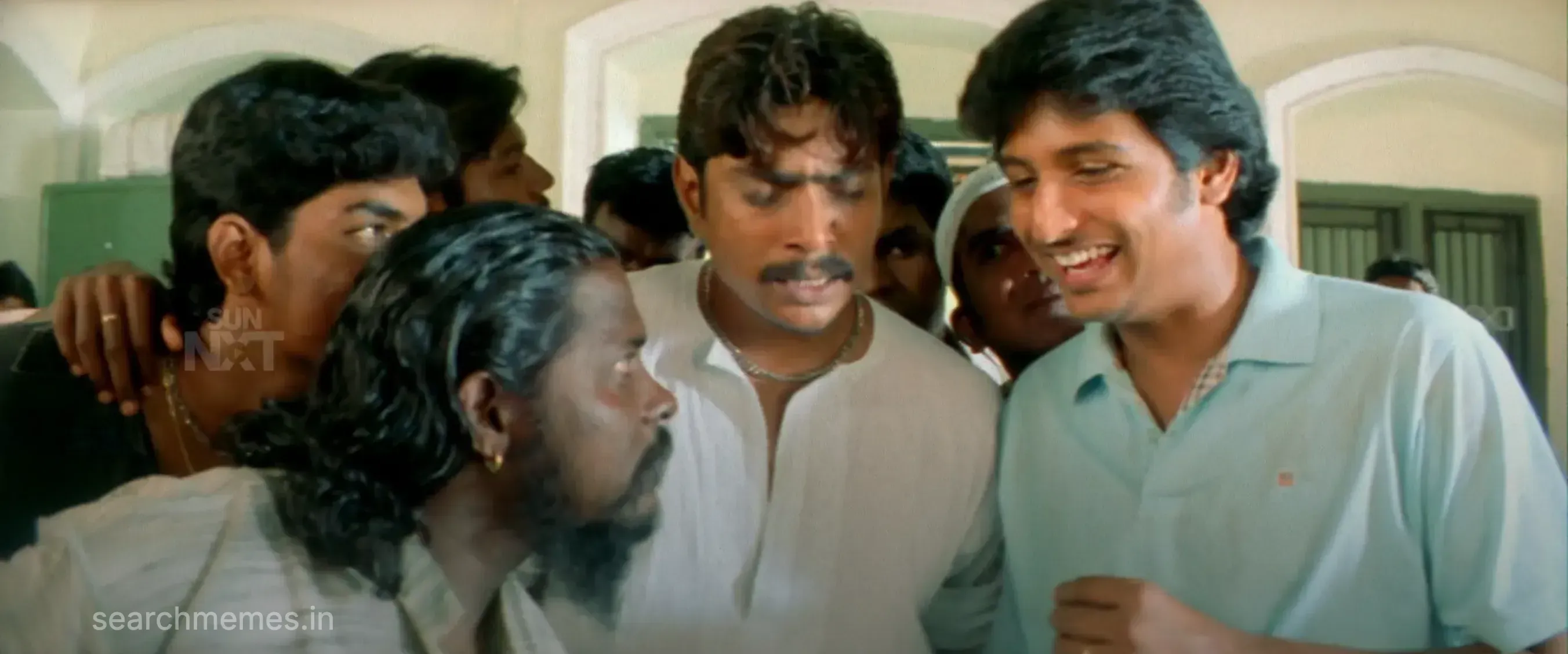 Jiiva smiling happily beside a tense group of friends at an office