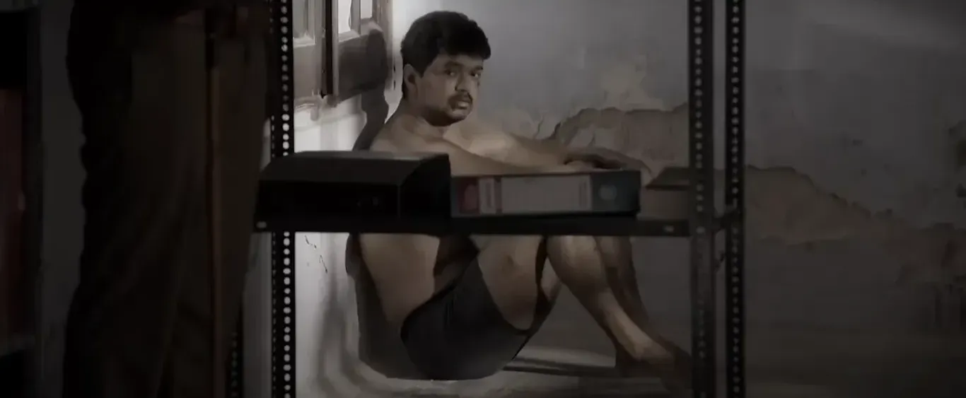 Vijay sitting huddled in a dark lockup corner clad in shorts