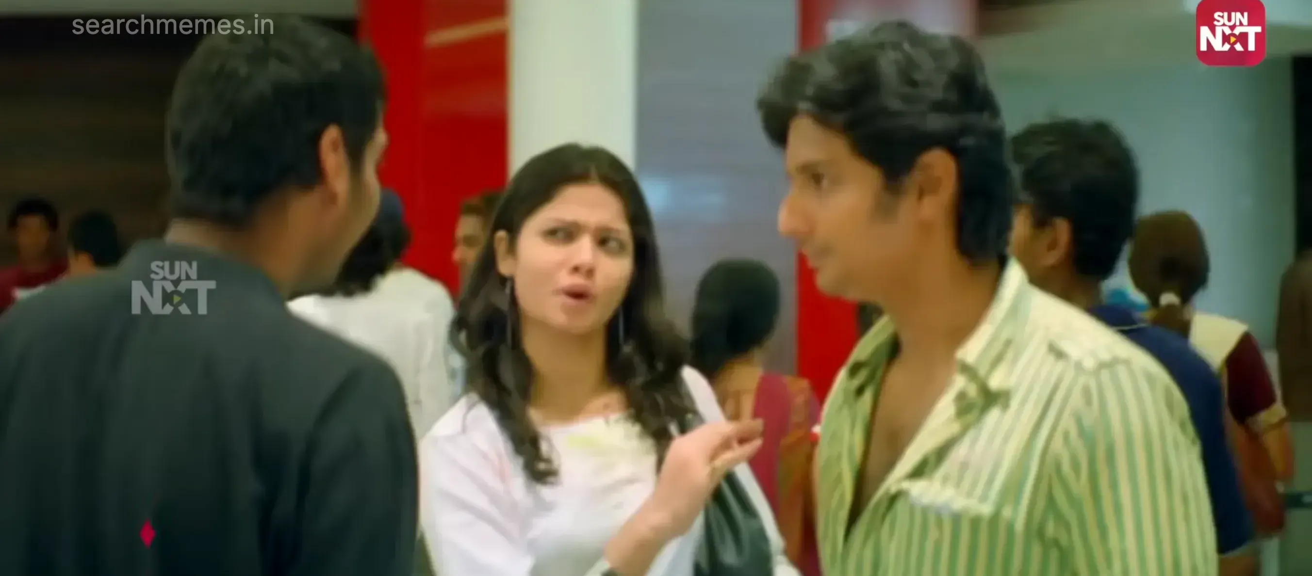 Jiiva gesturing toward Santhanam on a bike while speaking to a woman