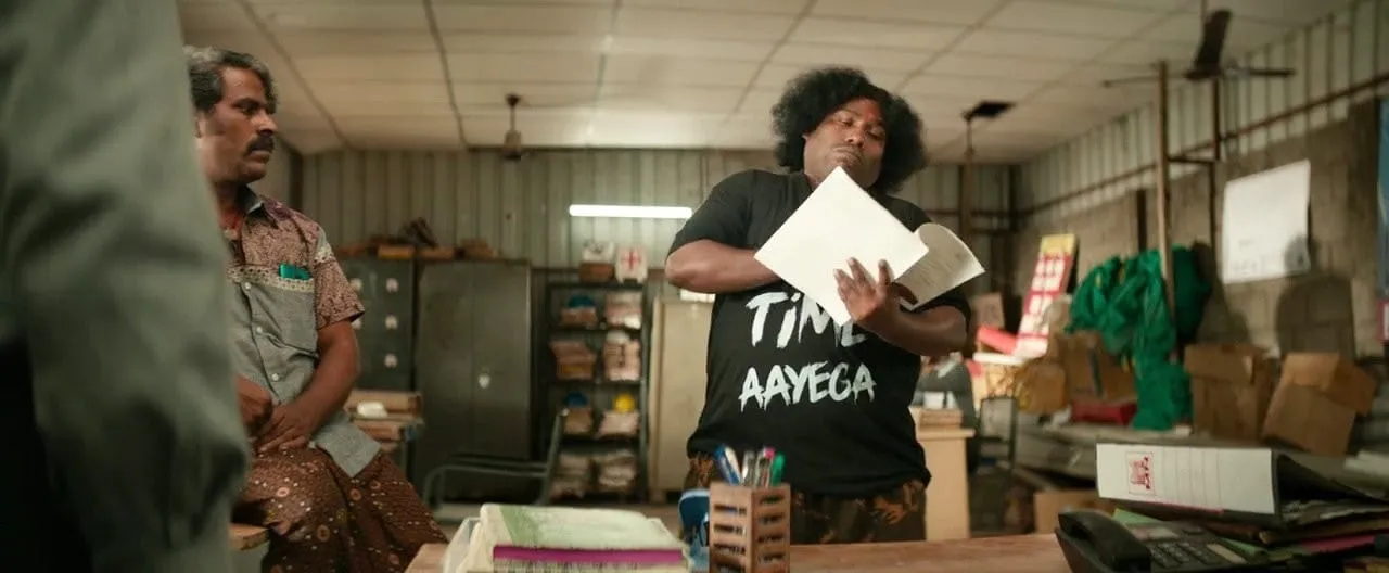 Yogi Babu holding up papers and staring at them with intense focus
