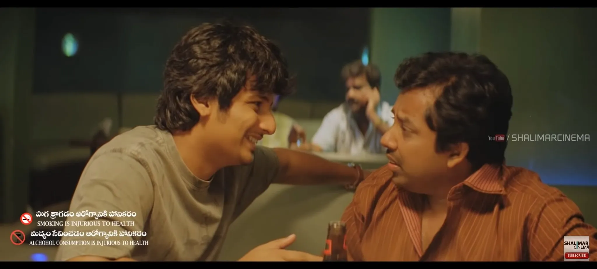 Jiiva grinning and speaking closely to Sathyan across a restaurant table