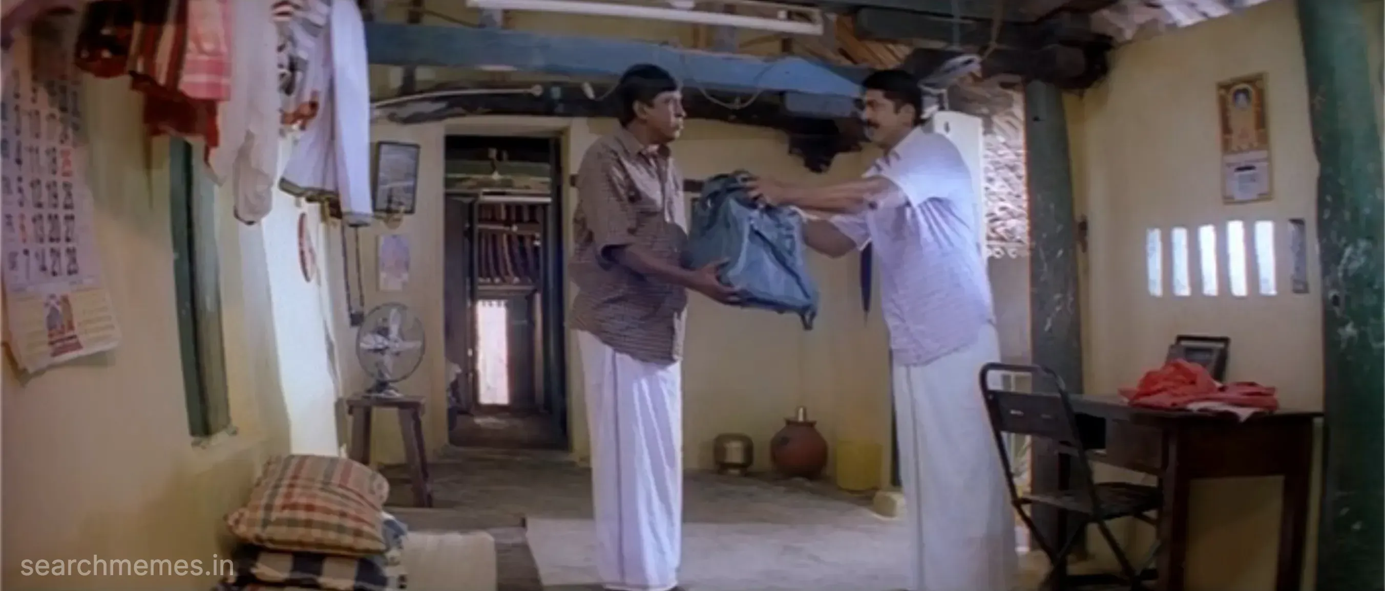 Vadivelu and Sarathkumar handing over a travel bag to each other indoors