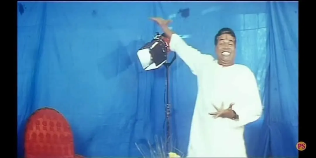 Vivek in white robes smiling and gesturing cheerfully on a blue stage set