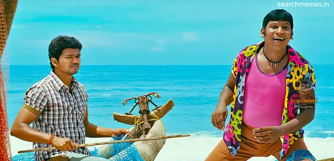 Vadivelu posing animatedly next to Vijay who sits on an anchored wooden boat by the seashore