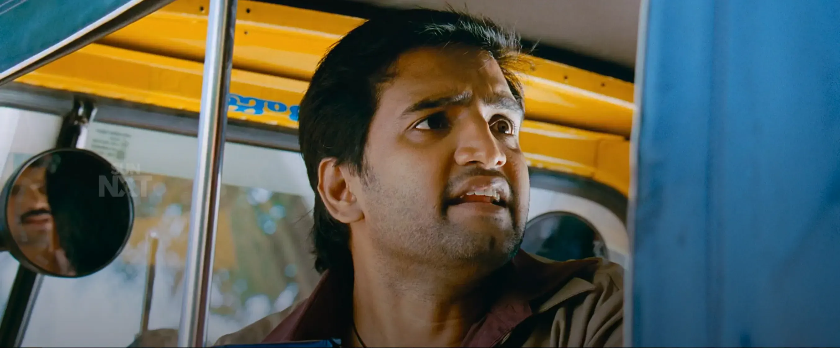 Karthi looking out of a yellow auto rickshaw with a shocked expression