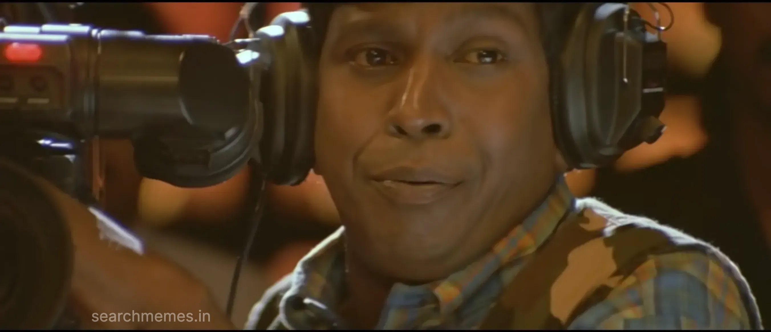 Vadivelu wearing headphones, trying to control his laughter while looking at the camera.